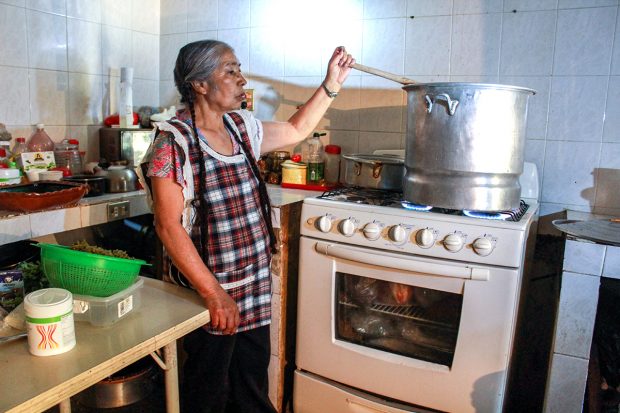 Romero Contreras prepara frijoles cuatatapa en su cocina. Cuando prepara el plato para su familia usualmente solo usa la mitad de las cantidades de la receta y usa una olla de barro, pero para la cantidad de guiso que está preparando para el festival se necesitan grandes porciones y una olla grande de aluminio. FOTO: Mayela Sánchez, GPJ Mexico.