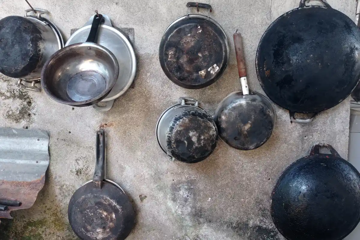 Sobre una pared cuelgan utensilios de cocina, entre ollas, sartenes, muy usados