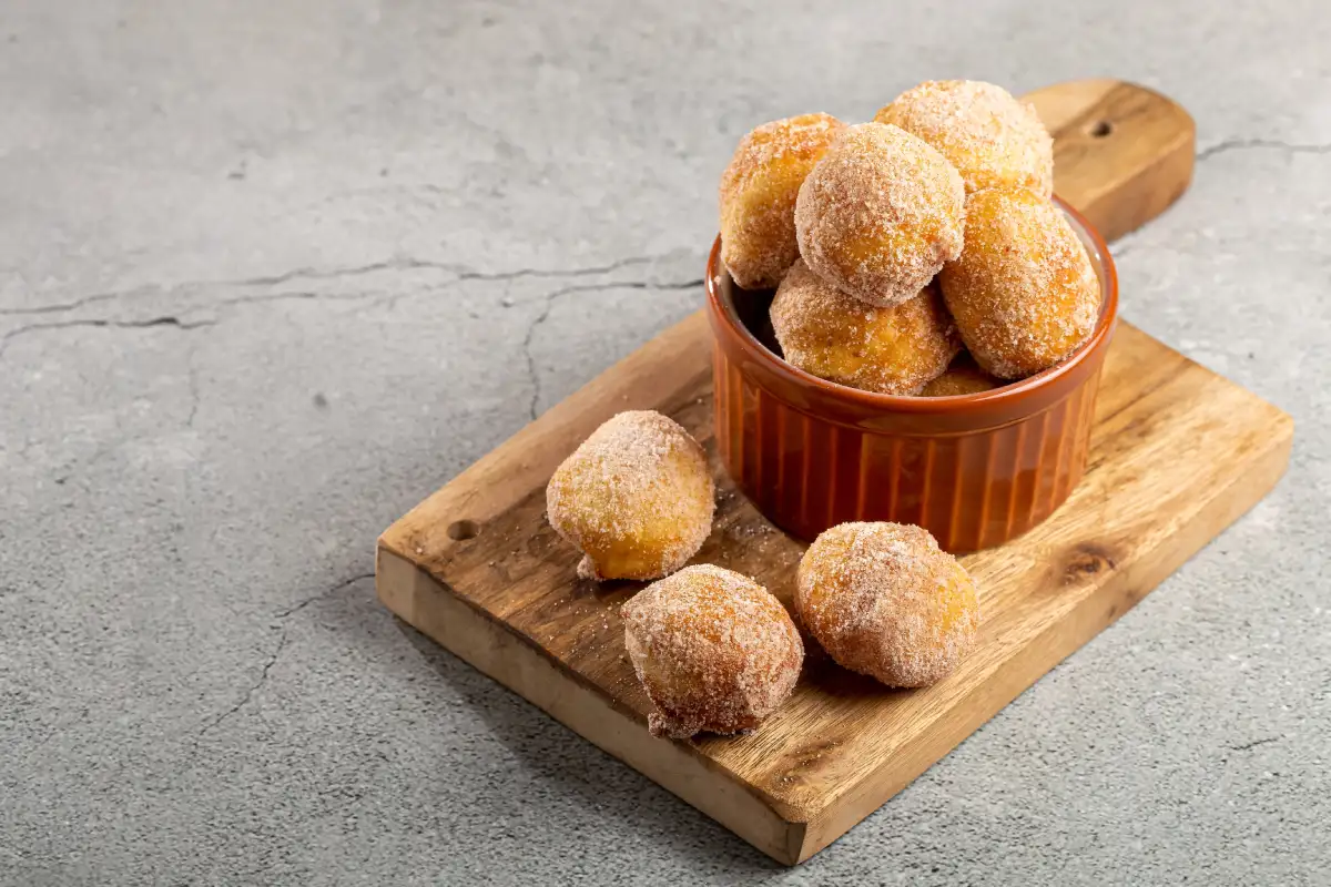 Sobre una tabla se encuentra un recipiente con buñuelos de viento al estilo de España, unas bolas de masa fritas y rellenas.