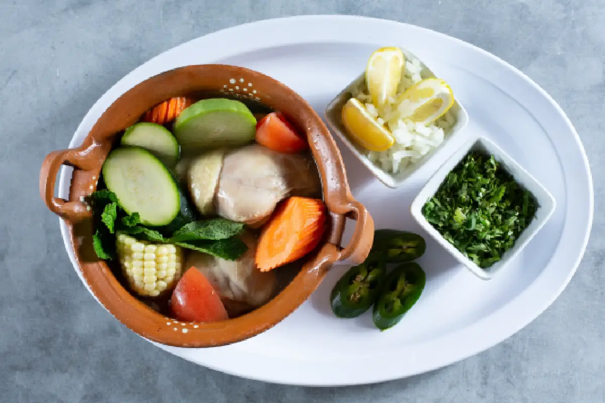 plato de caldo de pollo con verduras, chile, cilantro y limón
