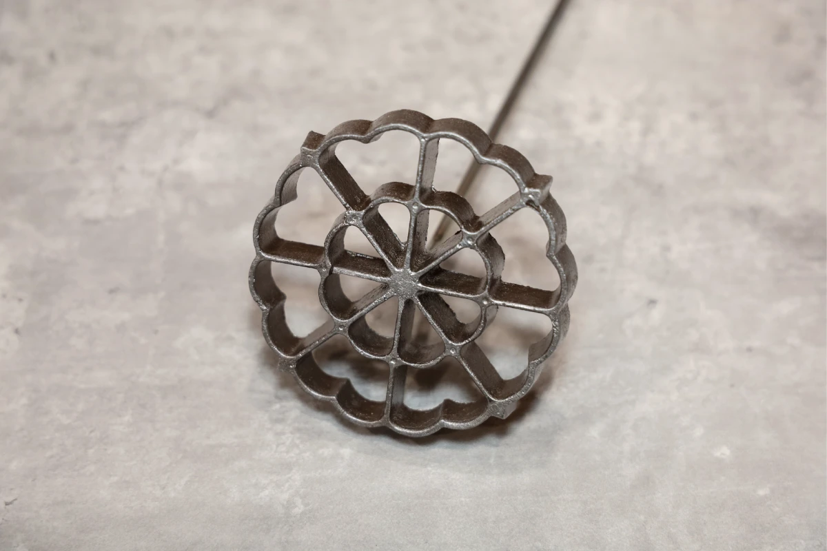 Sobre una mesa está un molde de hierro para hacer buñuelos de viento 