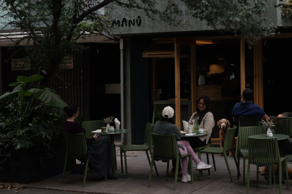 Exterior del restaurante Manū, ubicado en la Ciudad de México, con personas sentadas en sillas color verde.