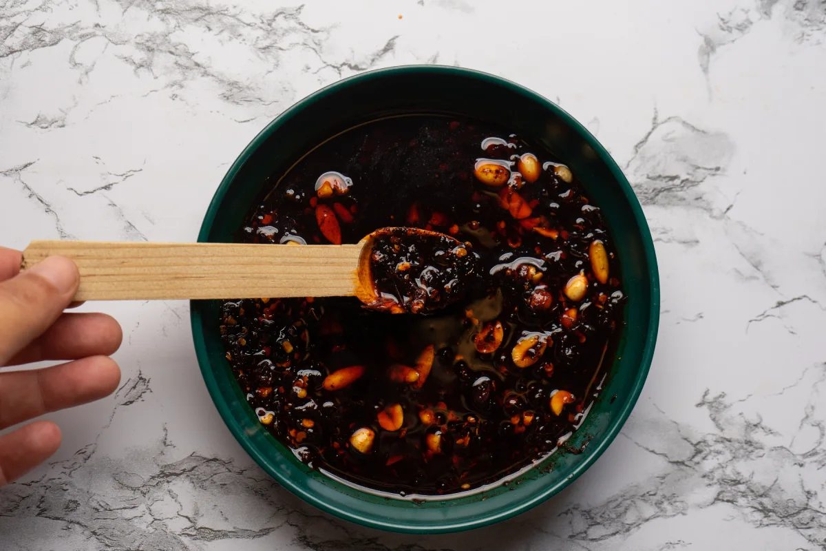 Una mano sostiene una cuchara de madera con salsa macha.