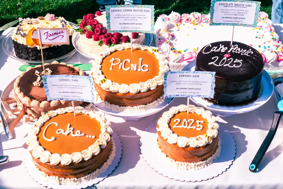 Sobre una mesa están colocados varios pasteles en lo que están escritos las palabras Cake Picnic 2025