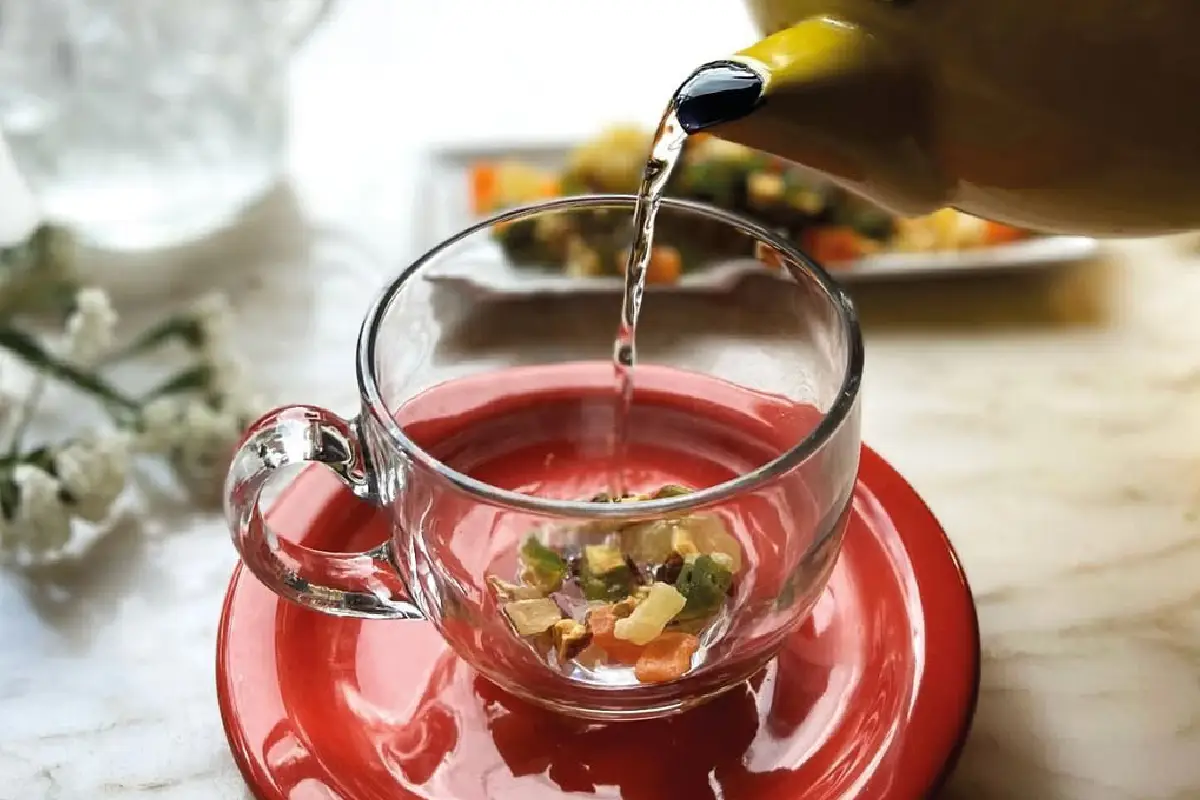 té sirviéndose en una taza transparente con hojas al fondo
