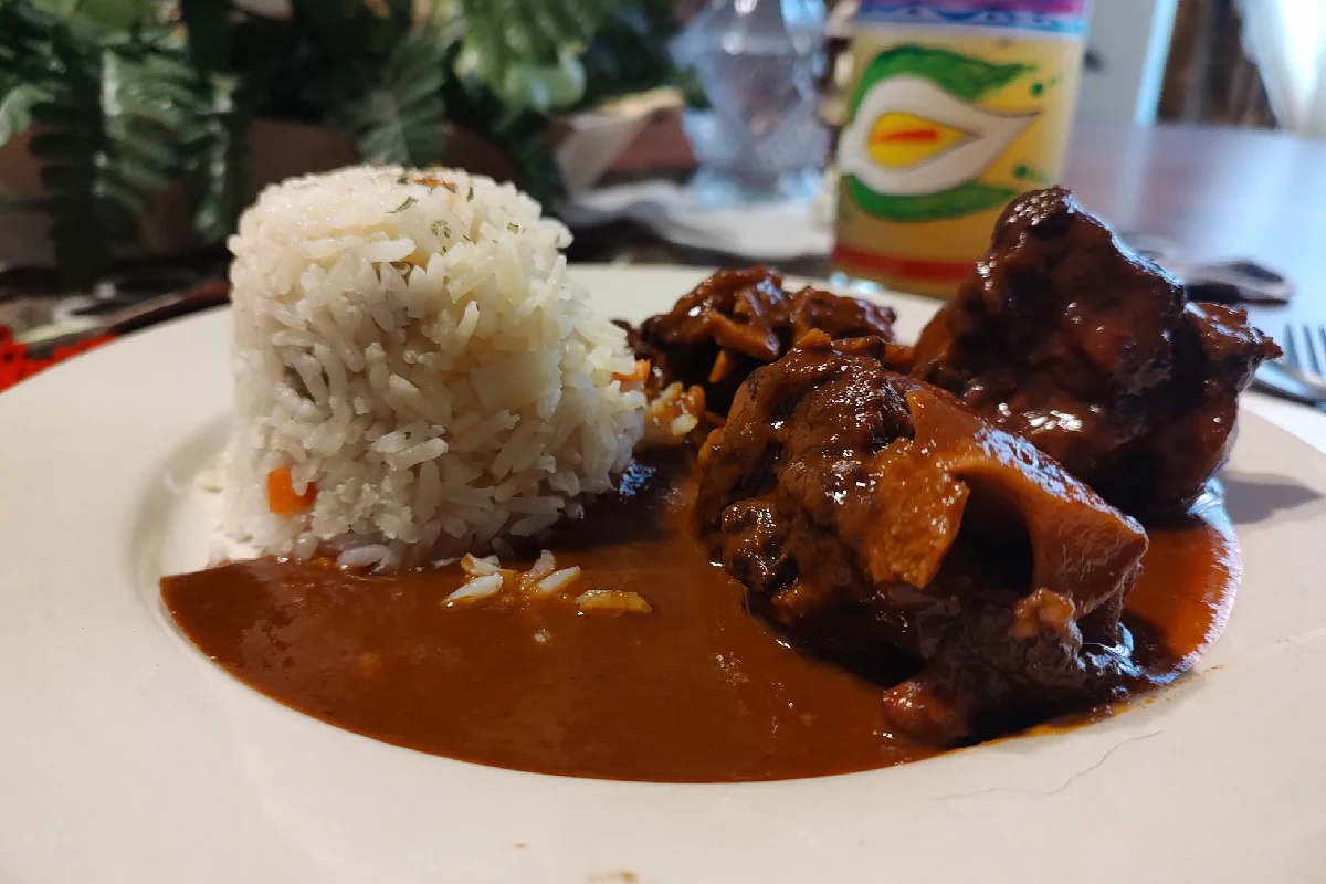 Un plato blanco contiene una pedazo de cola de res con adobo y lo acompaña una porción de arroz blanco.