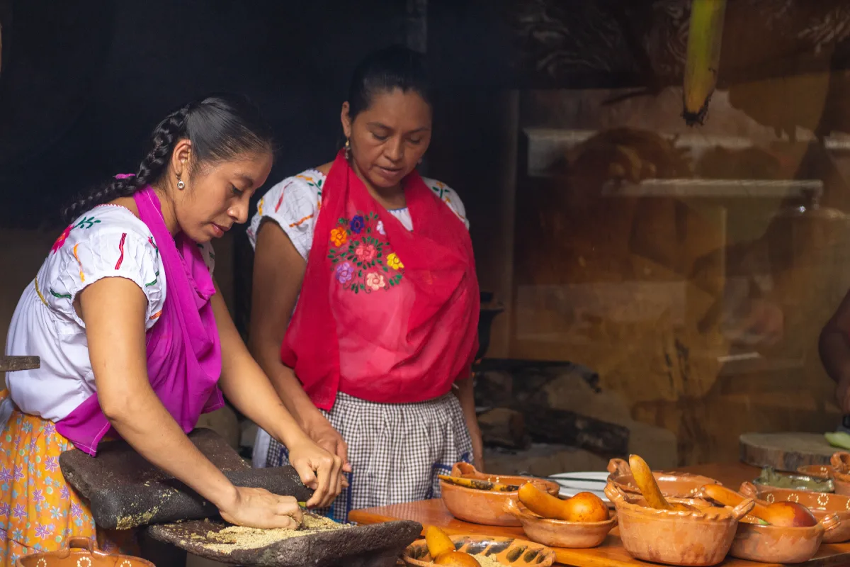 Dos mujeres tradicionales se encuentra moliendo semillas en un metate.