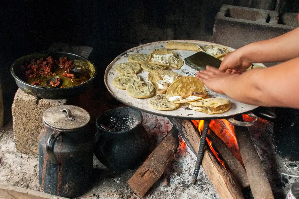 Las manos de una mujer cocinando comida tradicional mexicana con leña y un comal. 