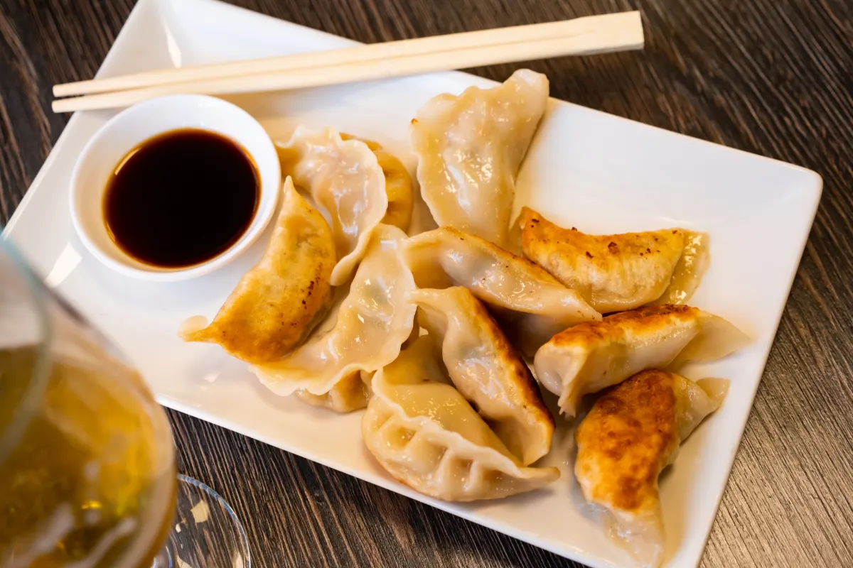 En un plato blanco están servido dumplings con carne servido con salsa de soja.