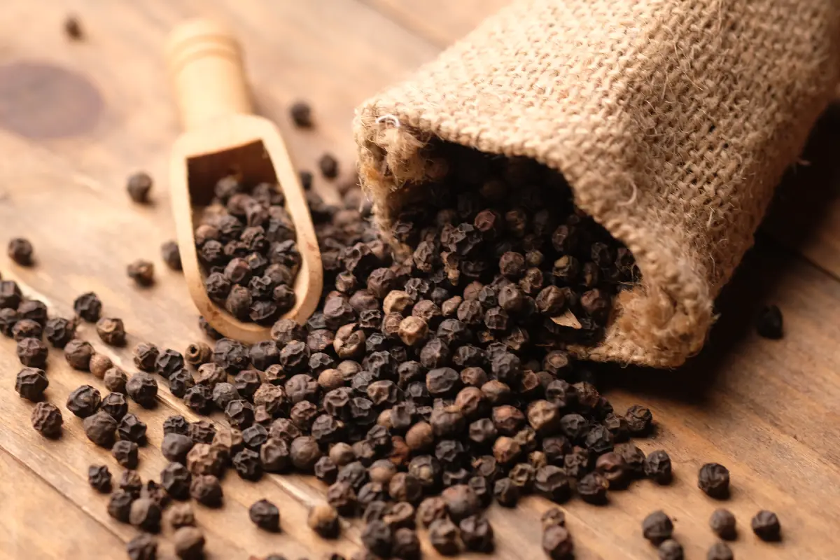 Un costal se encuentra abierto por donde salen pimientas negras regadas sobre el suelo.