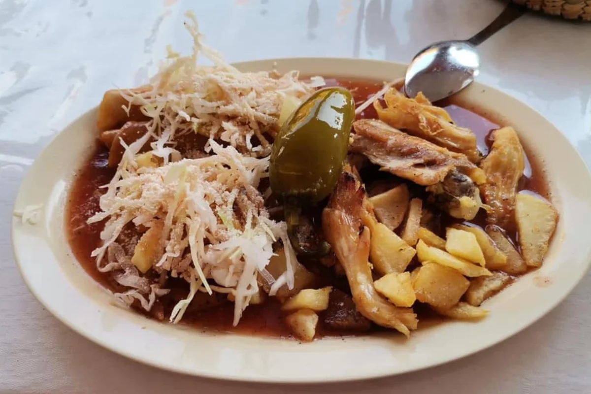 En un plato está servida una pieza de pollo frita con papas, col y chile jalapeño.