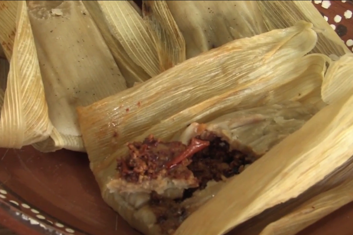 Un tamal abierto relleno de queso y chile, con hoja de maíz.