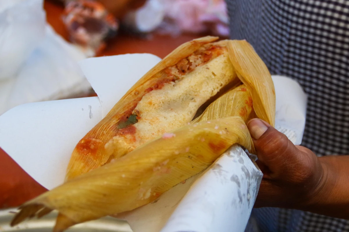Una mano sostiene un tamal de rajas con queso.