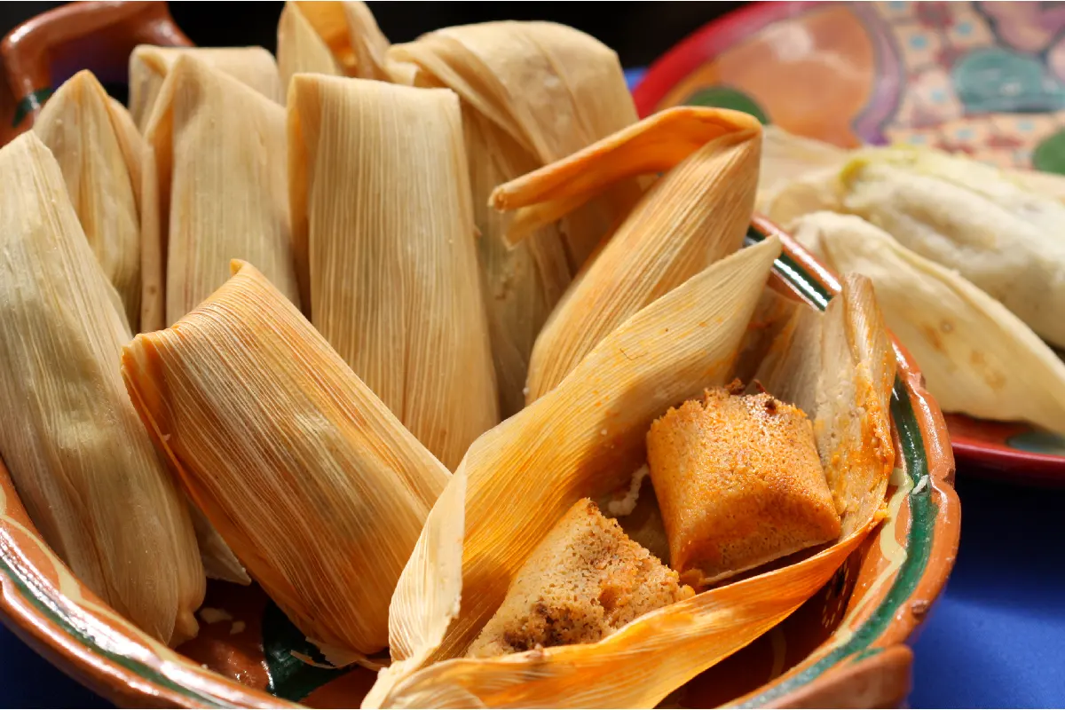 Dentro de una olla de barro se encuentran varios tamales y uno está abierto.