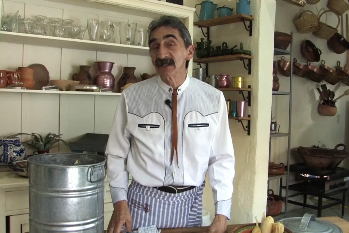 En una cocina se ecuentra parado el chef Yuri de Gortari el cual lleva una camisa blanca un mandil de cocina amarrado en la cintura.
