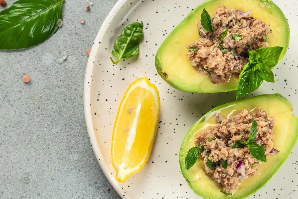 Aguacate relleno de atún sobre un plato blanco acompañado de limón amarillo.