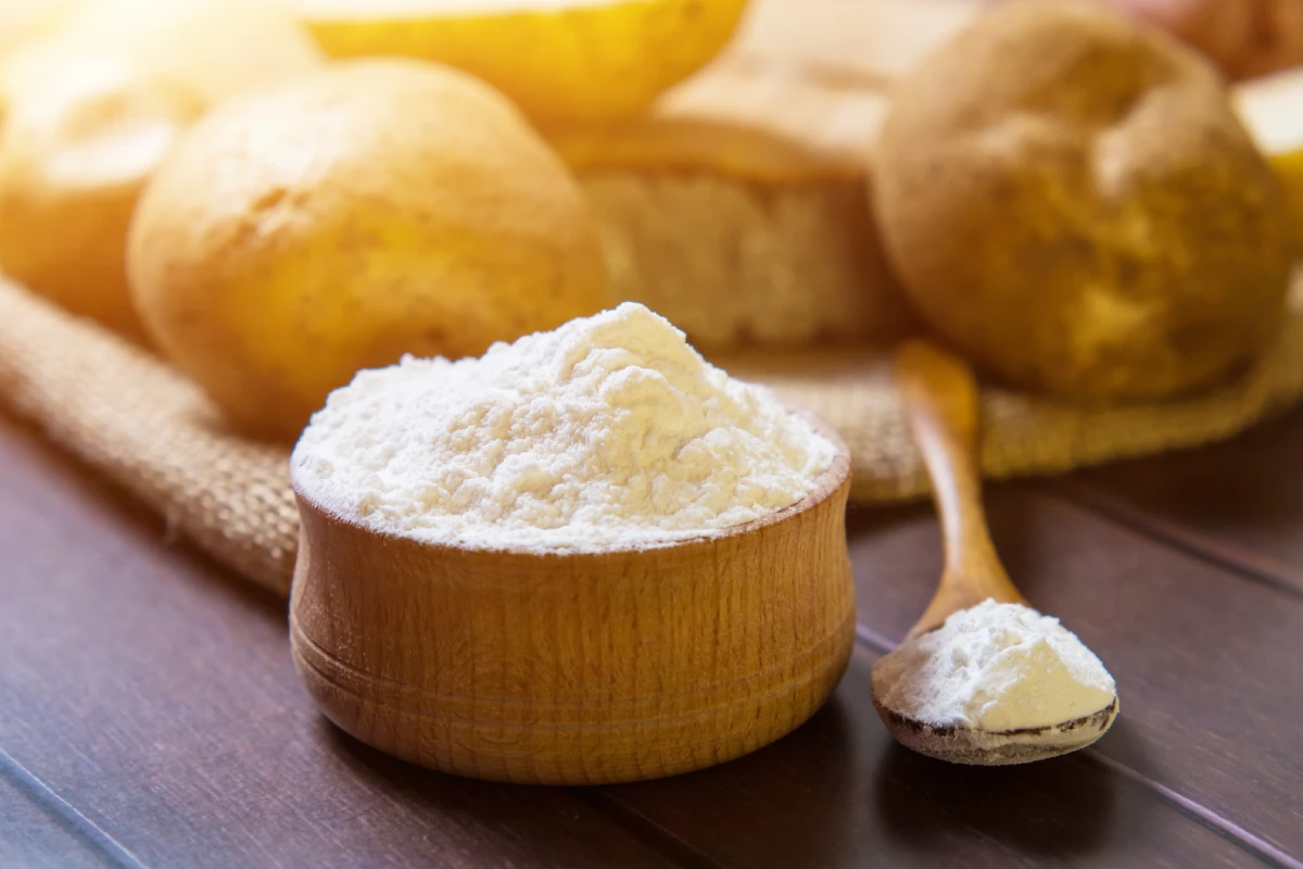 Al fondo hay papas y al frente un recipiente y cuchara con maicena