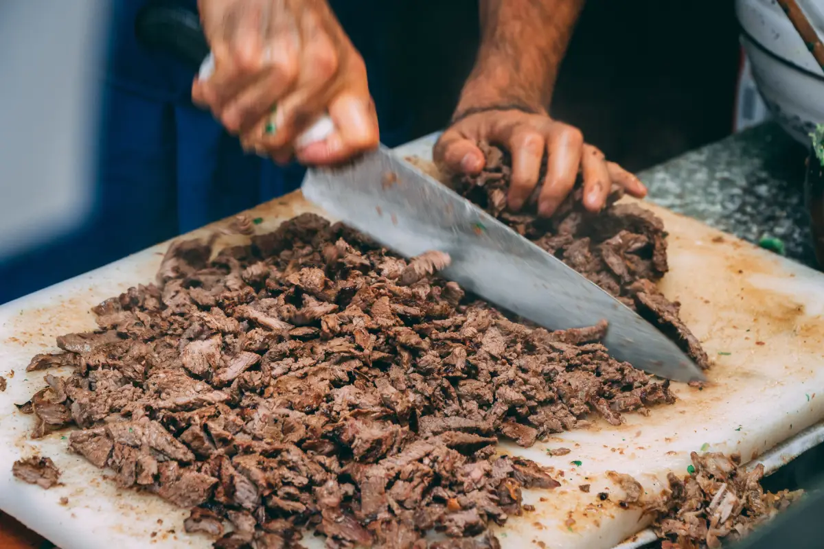 Acercamiento de un chef cortando carne asada en una tabla de cortar de plástico con un cuchillo.