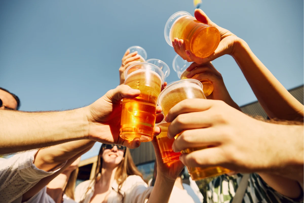 Un grupo de personas sostienen vasos de plástico con cerveza clara.