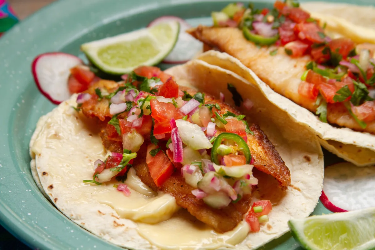 En un plato están servidos tacos tradicionales mexicanos de pescado con pico de gallo.