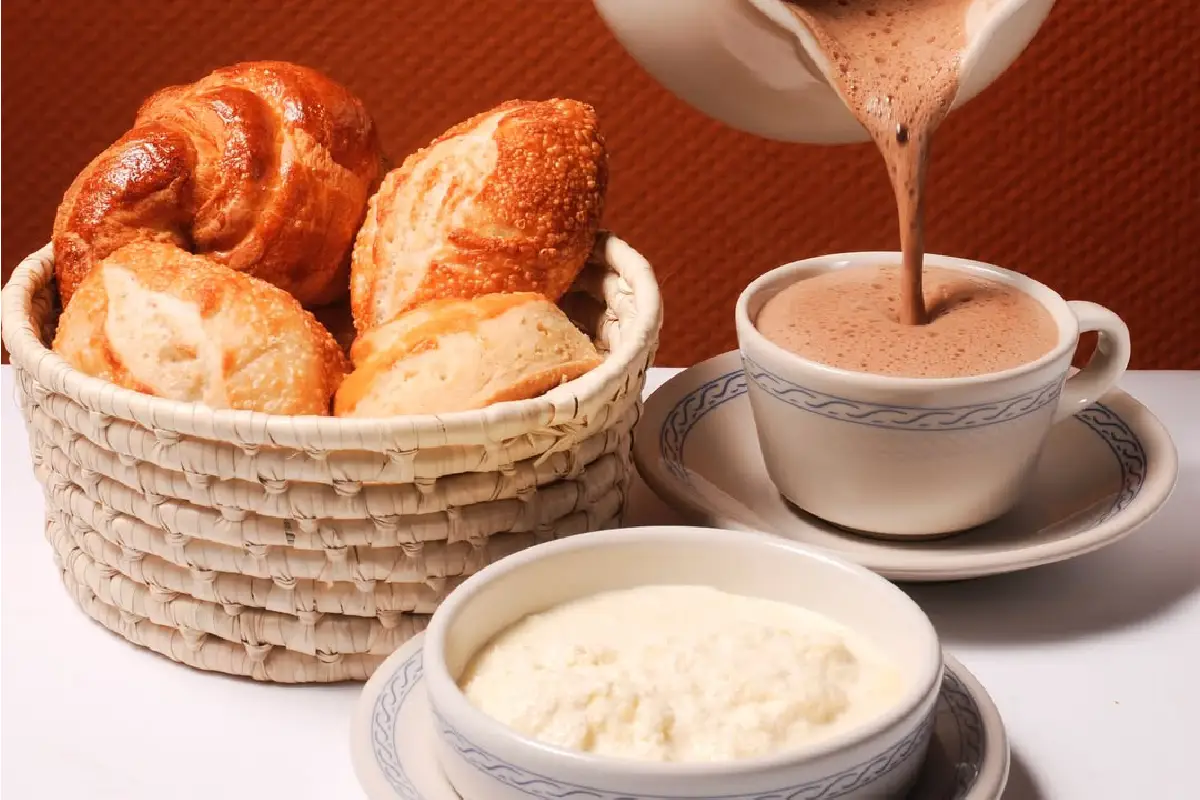 mesa con chocolate caliente y pan recién hecho y nata