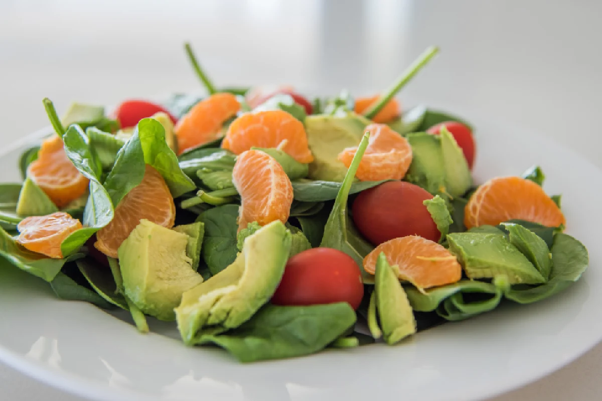 En un plato blanco se encuentra una ensalada de espinacas con mandarina, aguacate y jitomate cherry.
