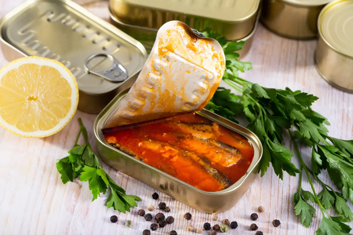 Una lata de sardina a medio abrir junto con ingredientes para preparar sardinas a la mexicana.