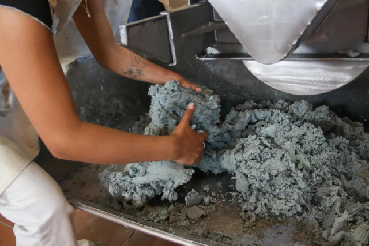Una mujer remueve la masa azul que cae de un máquina para hacer tortillas