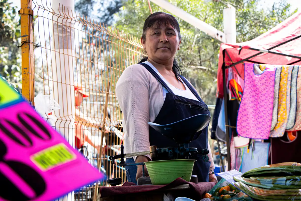 Mujer posa detrás de su puesto de verduras colocado en un tianguis.